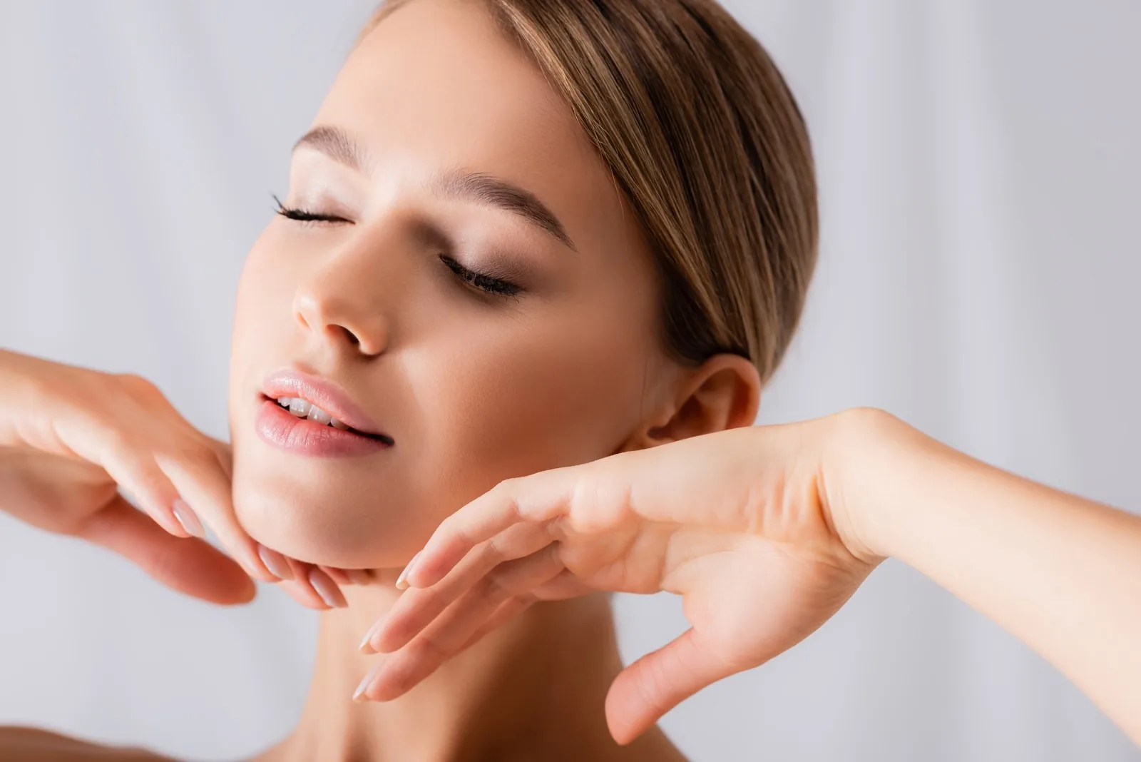 Close-up of a woman with her eyes closed framing her face with both hands