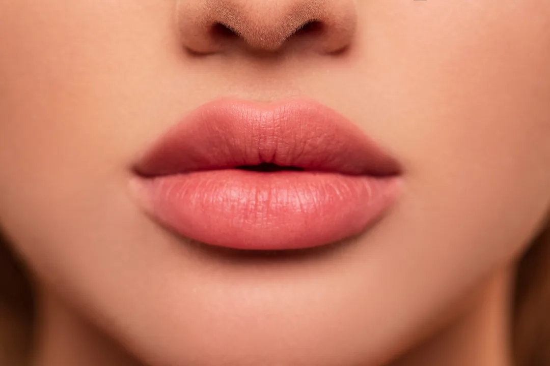 Close-up of a woman's full pink lips and the tip of her nose