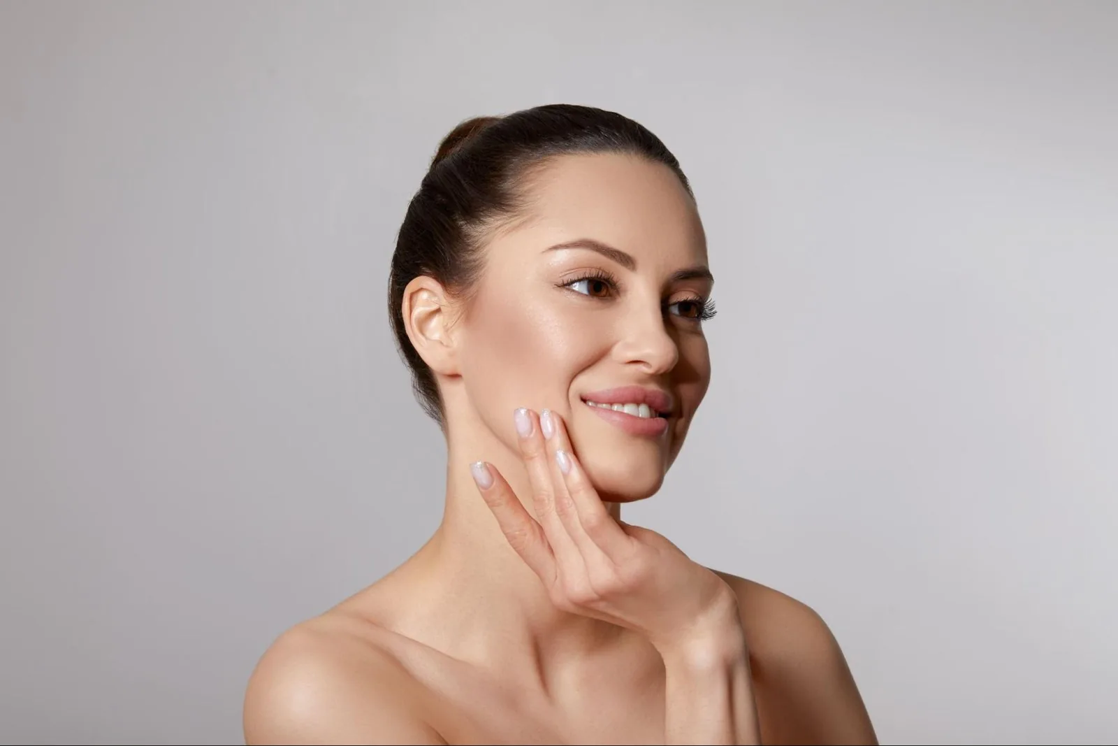 A woman with her hair pulled back smiling and resting fingertips on her cheek