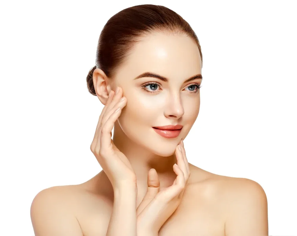 A woman with her hair pulled back touching her cheek and chin against a white background
