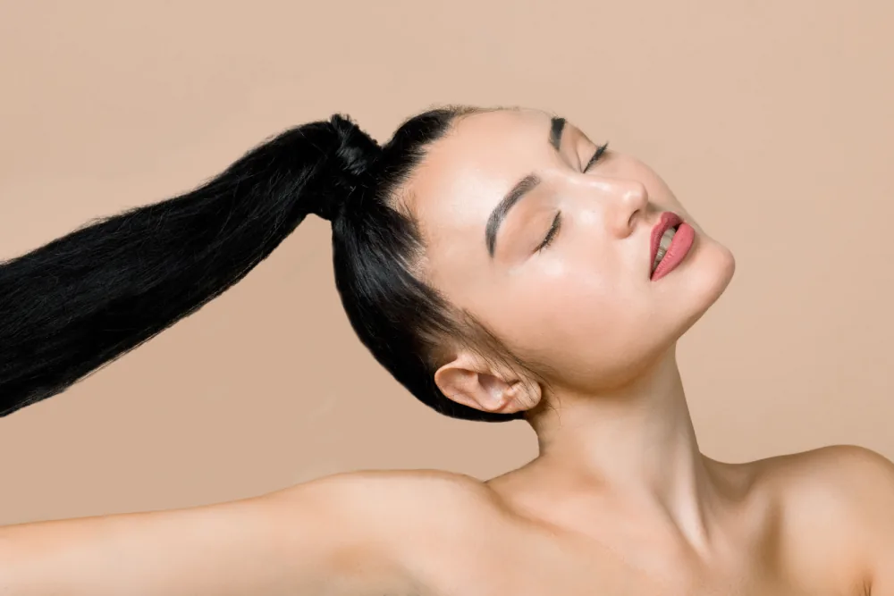 A woman with eyes closed and a long black ponytail held up in the air