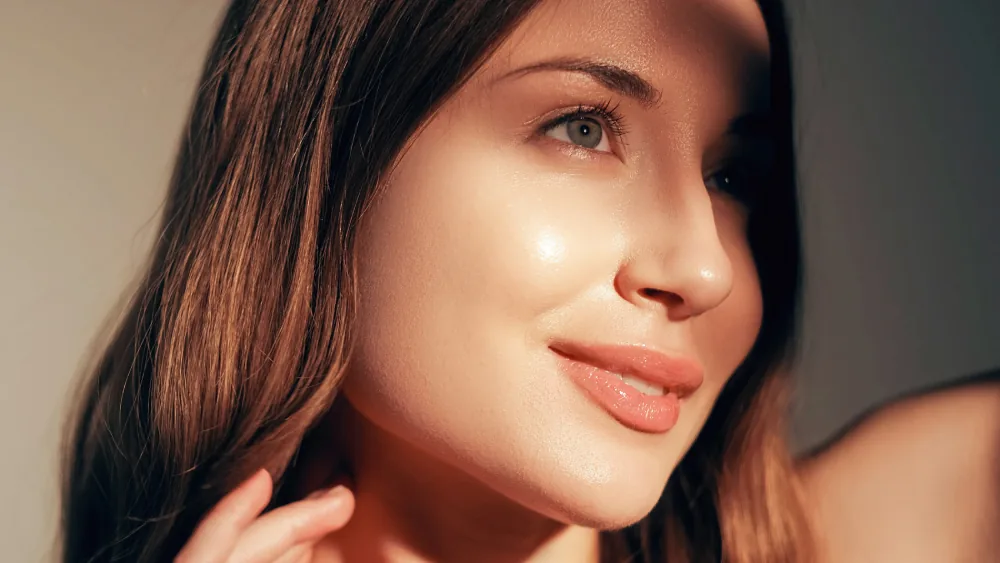 Close-up of a smiling woman with long brown hair in warm light looking to the side