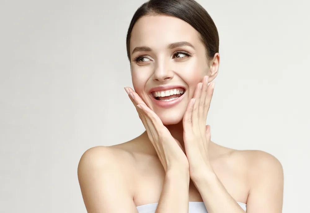 A laughing woman with her hair pulled back holding both hands to her cheeks