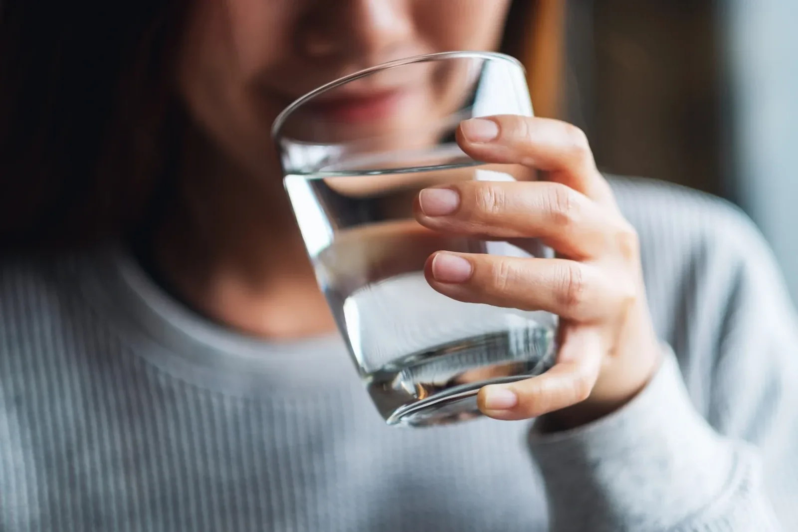 Close-up of a woman in a grey sweater drinking from a glass of water