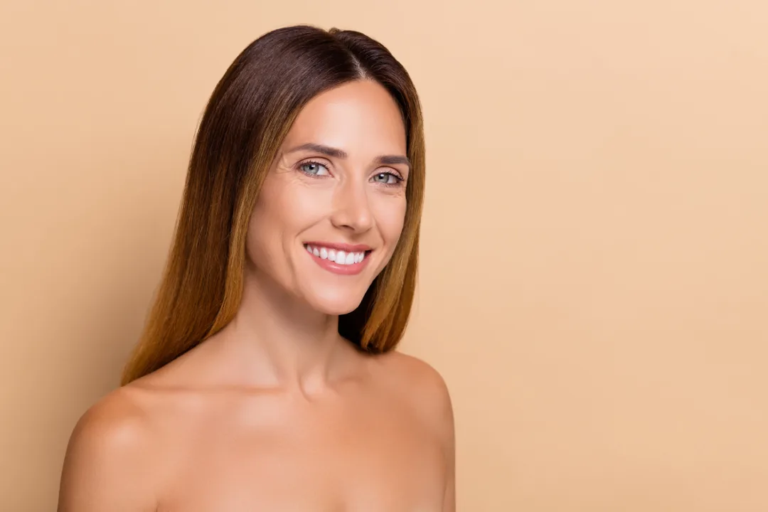 A smiling woman with long brown hair and bare shoulders against a beige background