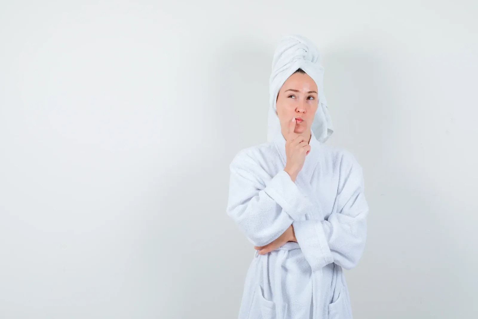 A woman in a bathrobe and towel turban looking up with a finger on her lips