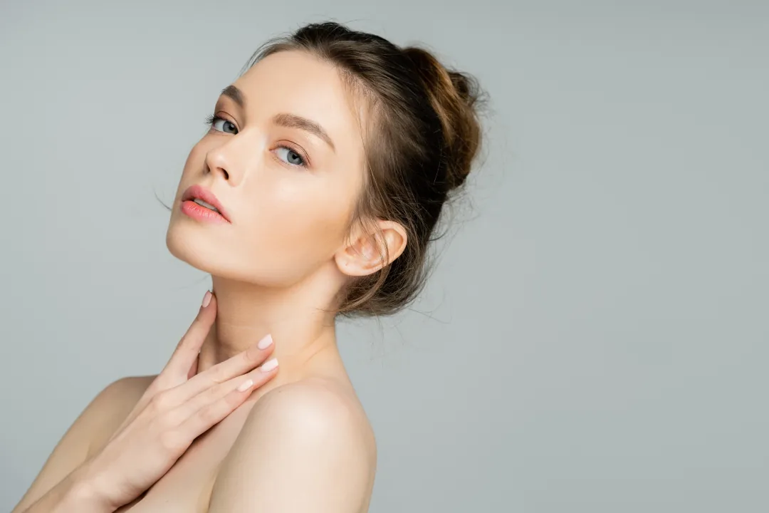 A woman with her hair in a bun touching her neck and looking at the camera