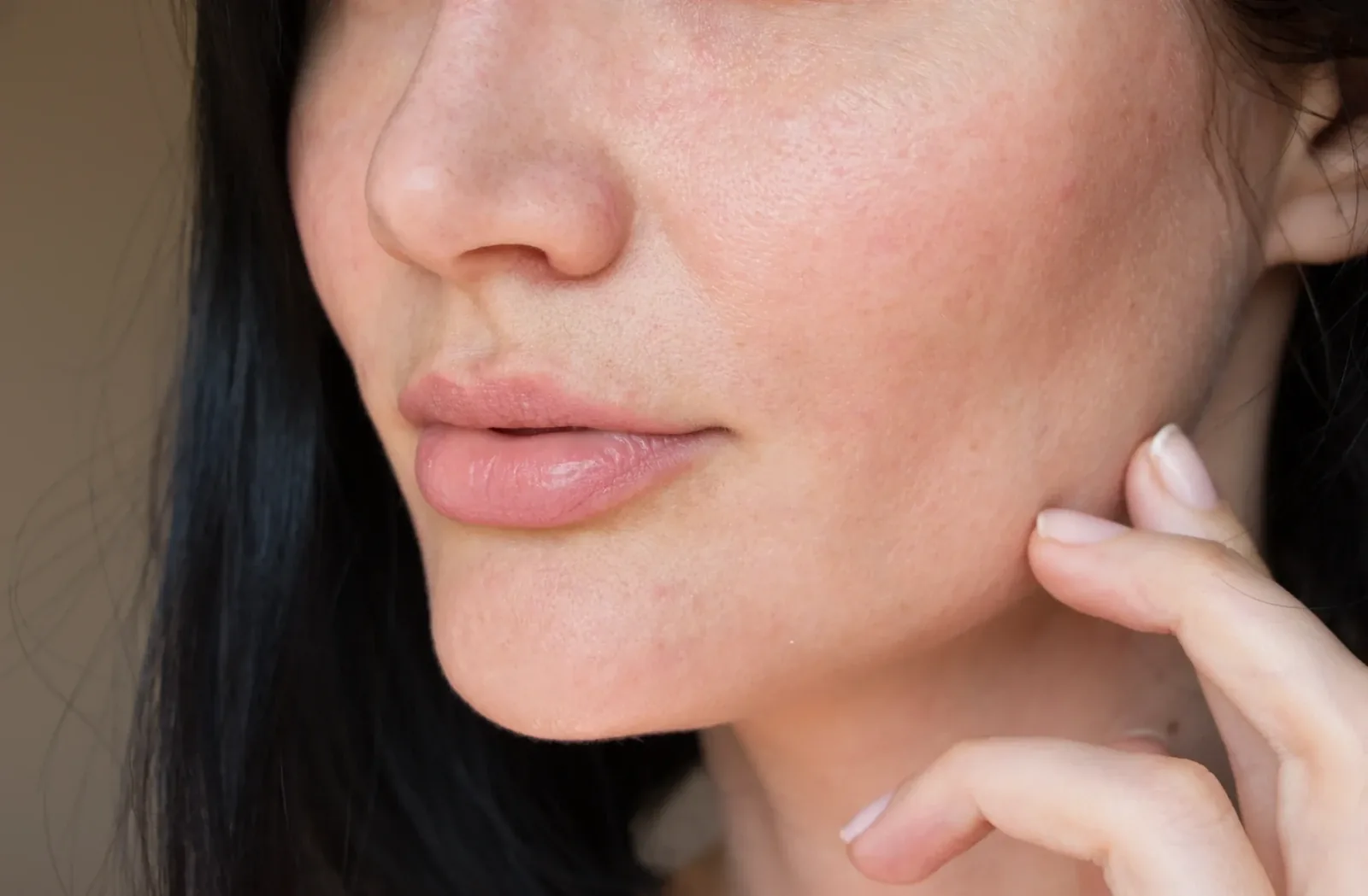 Close-up of a dark-haired woman's cheek and lips with a fingertip resting on her jaw