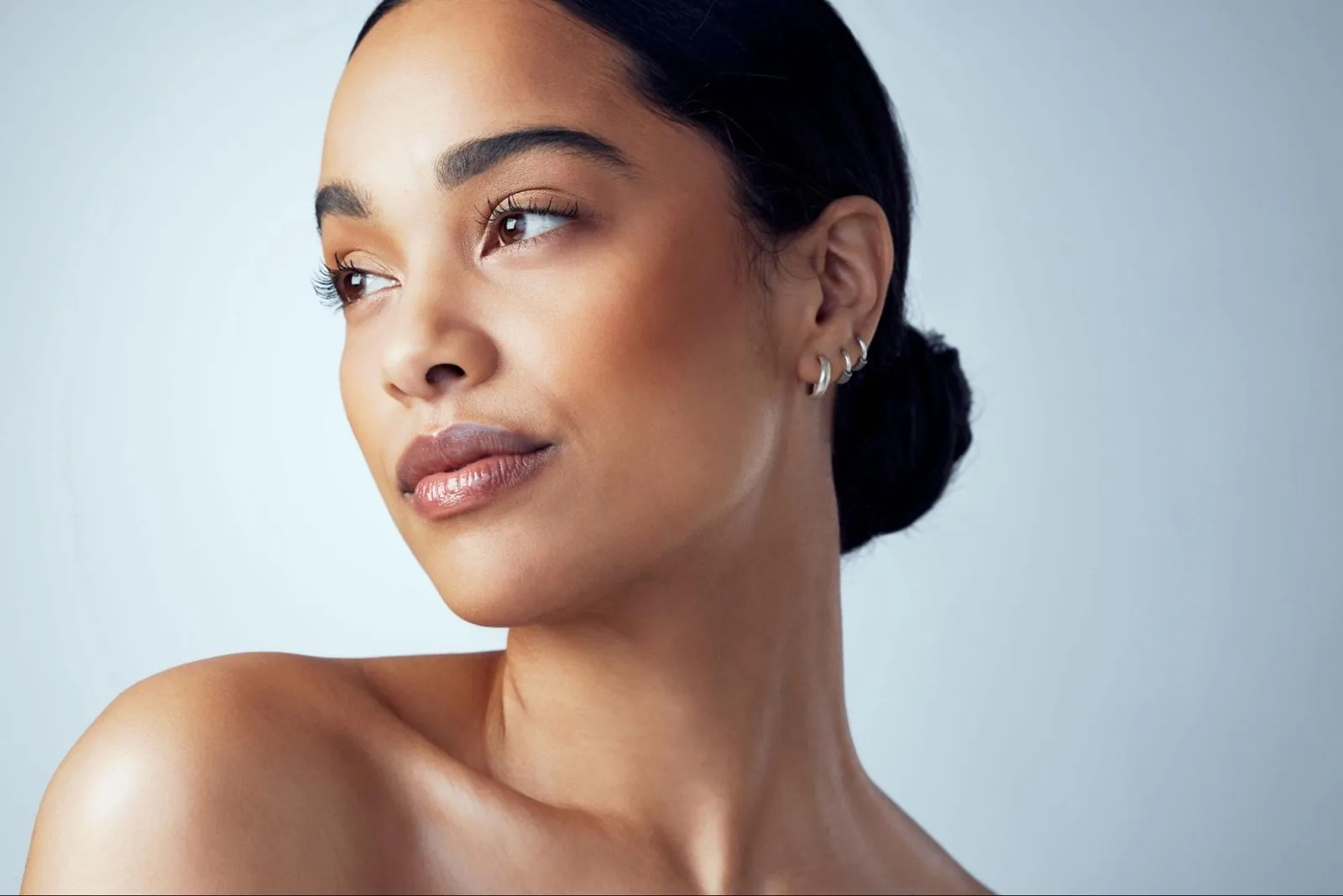 A woman with a sleek low bun and small hoop earrings looking to the side