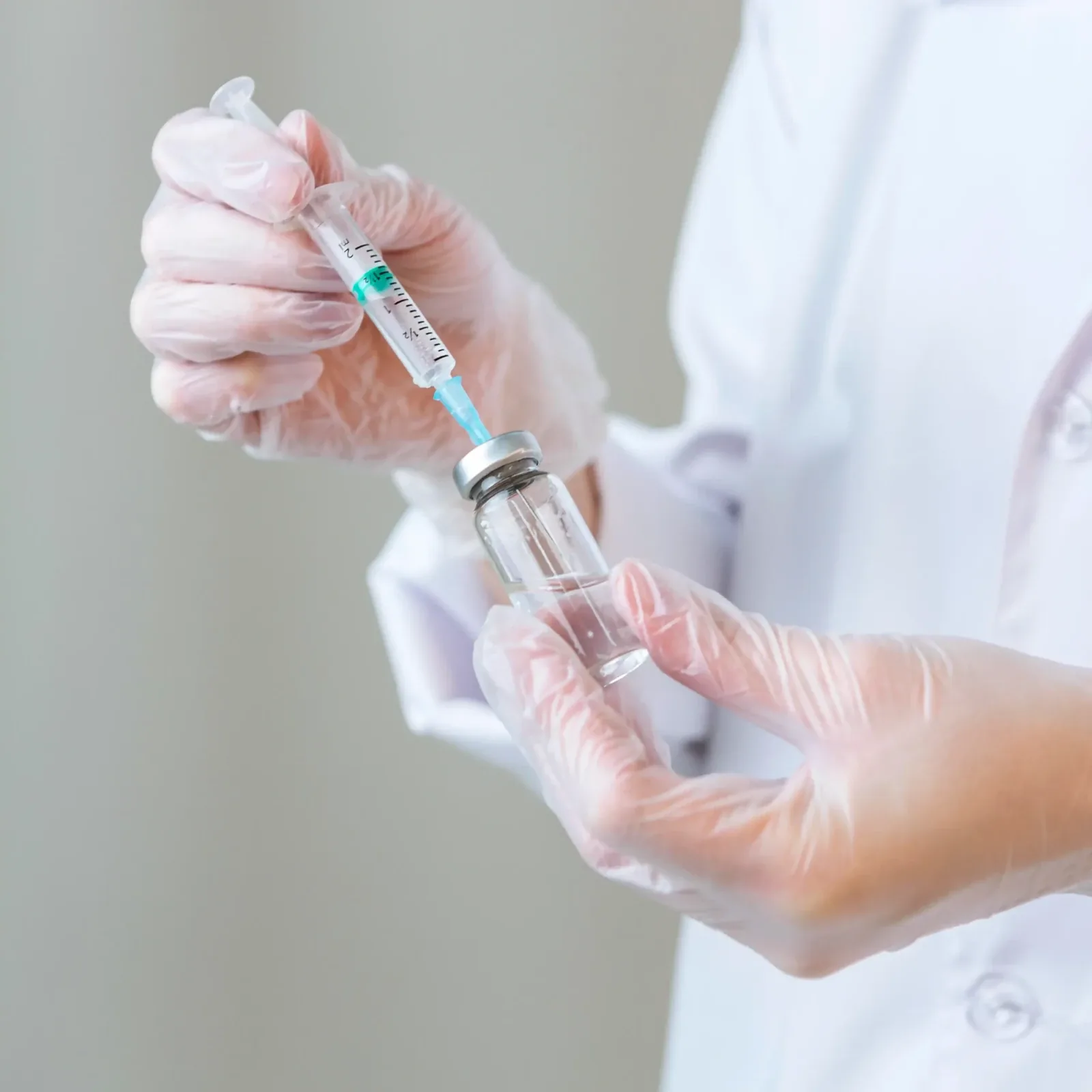 Gloved hands drawing liquid from a small glass vial into a syringe