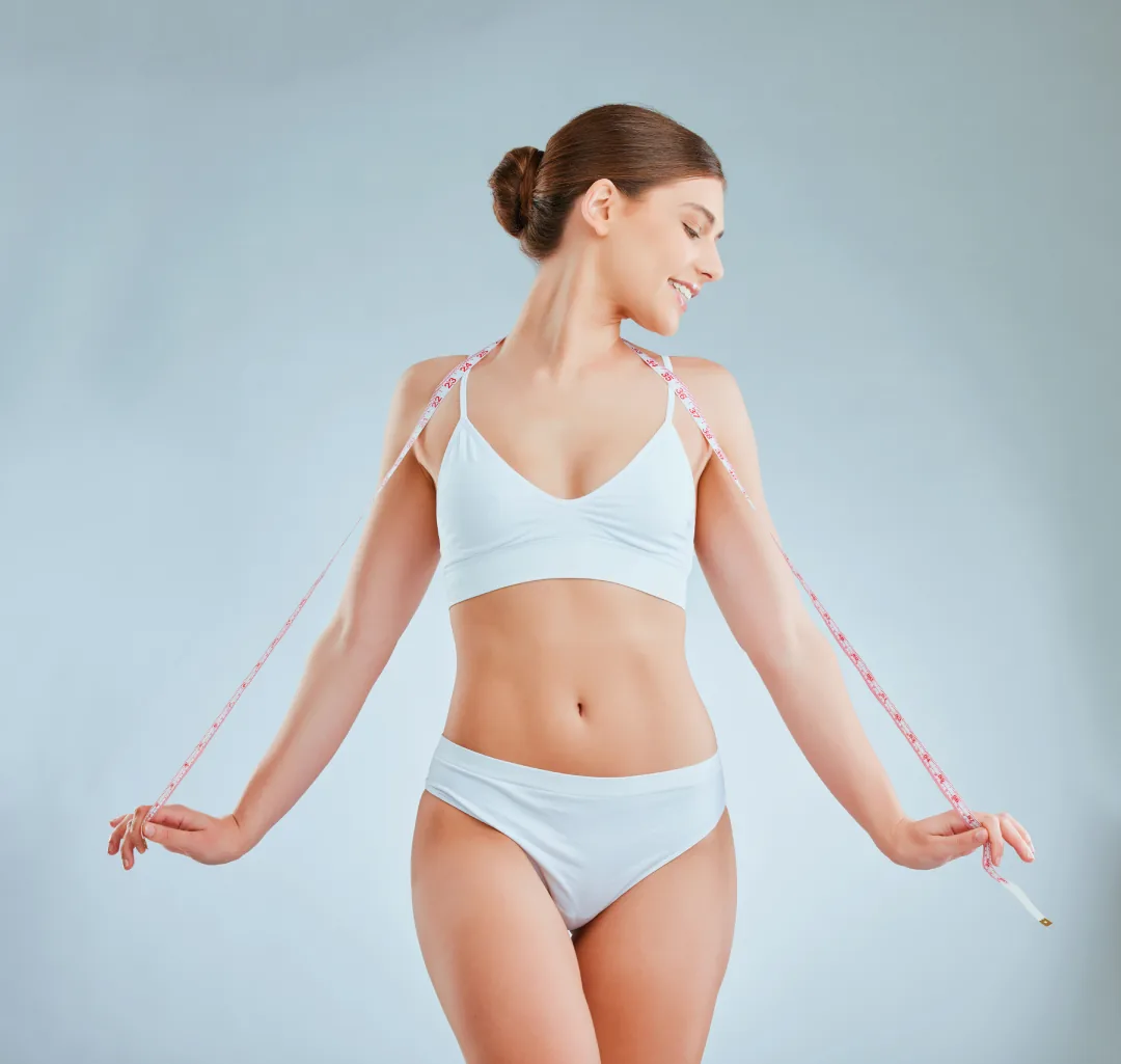 A smiling woman in white underwear holding a tape measure draped over her shoulders