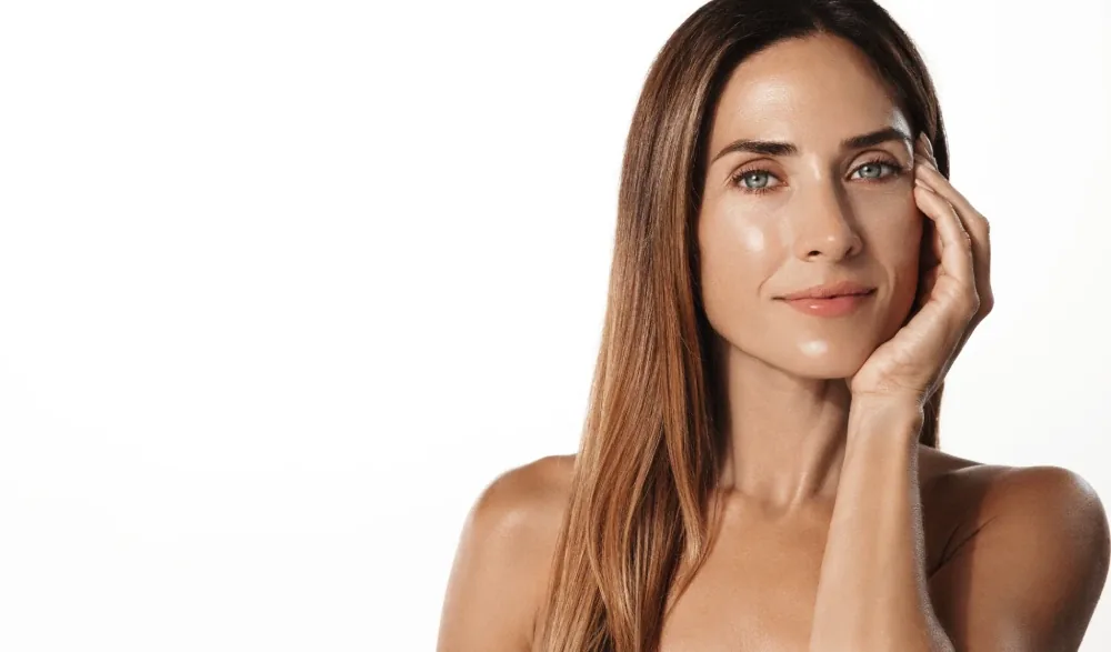 A woman with long light brown hair resting her cheek on her hand against white