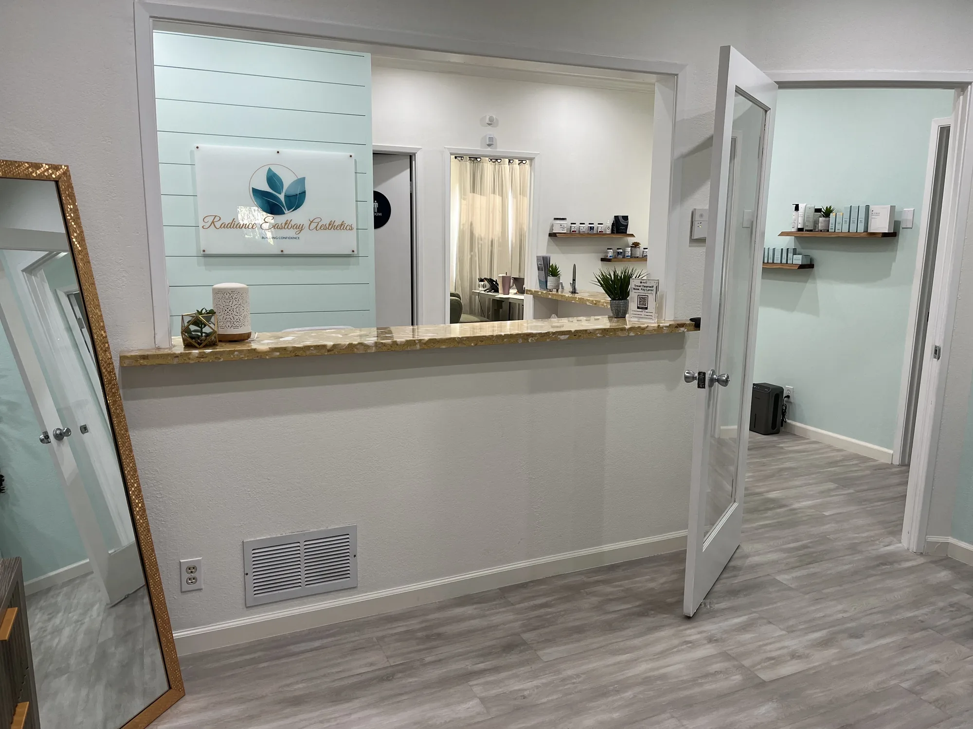 The reception at Radiance East Bay Aesthetics in Pleasanton, with the leaf logo on the shiplap wall, the front desk and the hallway to the treatment rooms